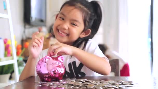 Nettes Mädchen steckt zu Hause Münzen in Sparschwein - Filmmaterial, Video