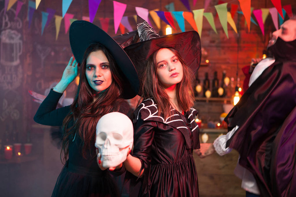 Женщины в костюмах ведьм на Хэллоуин стоят с человеческим черепом в руках
 - Фото, изображение