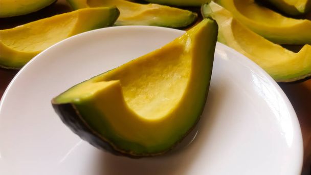 Tasty, quarter avocado slice on white plate, more quarter slices in the background - Valokuva, kuva
