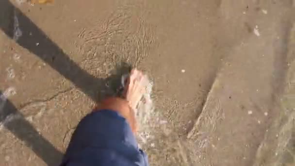 Miehen jalat kävelevät kirkkaaseen matalaan veteen.Miehen jalat, kunnes hän kävelee paljain jaloin matalassa merivedessä. Kuva - JPEG-videokoodekki
             - Materiaali, video