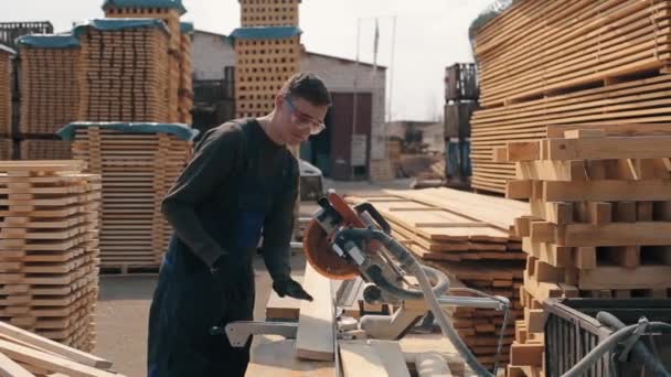ενήλικος ξυλουργός εργαζόμενος φορώντας γυαλιά κατασκευής με μηχανή κοπής ξύλου. άνθρωπος κόβει ξύλινες σανίδες. - Πλάνα, βίντεο