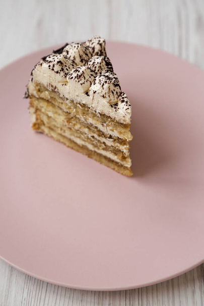 Un pedazo de pastel de tiramisú en un plato rosa sobre una surfa de madera blanca
 - Foto, imagen