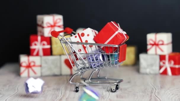 A lot of gifts fall on top of a small toy trolley with gifts. Shopping cart full of New Year's gifts. New Year's and Christmas. - Кадри, відео