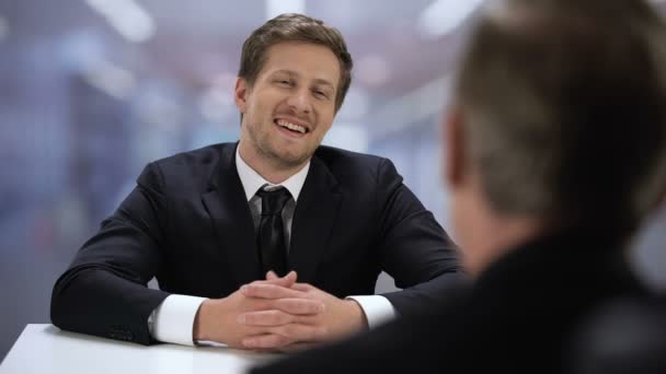 Joven hombre de negocios hablando con pareja adulta durante la reunión, riendo y bromeando
 - Metraje, vídeo