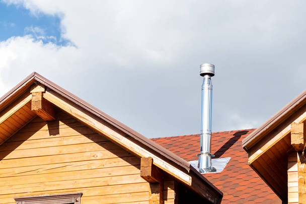 現代の木製のビームコテージヴィラの家の屋根にステンレス鋼の煙突パイプ。家庭用暖炉と暖房排気システム - 写真・画像
