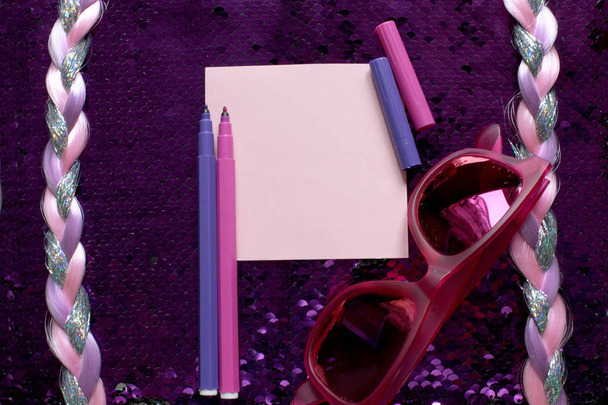 ein Blatt Papier zum Schreiben und rosa und lila Filzstifte und Sonnenbrillen auf leuchtend rosa Hintergrund Stoff mit Pailletten glänzt und schimmert und ein Zopf aus glänzenden Fäden, freier Platz für Platten - Foto, Bild