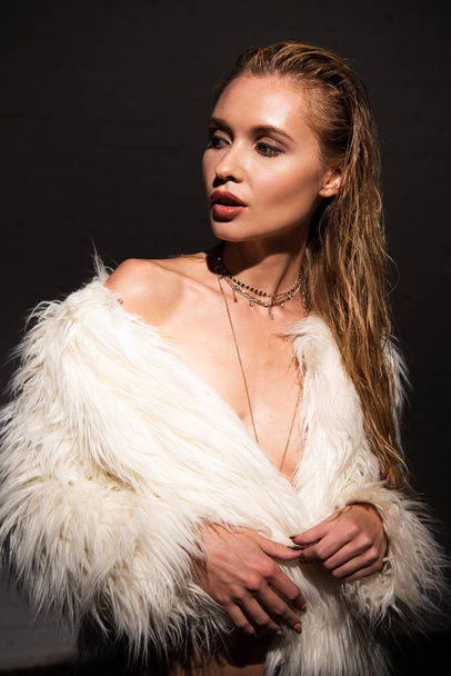 sexy naked young woman in white faux fur coat isolated on black - Photo, Image