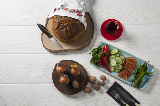 верхний вид сервировки стола со свежим хлебом, яйцами и нарезанными овощами на тарелке
 - Фото, изображение
