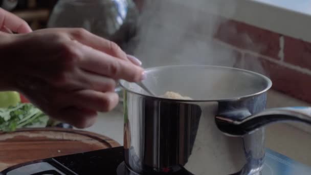 De pot is op de kachel in de keuken. Vrouwelijke hand roert PAP. Kokend water stijgt stoom. - Video