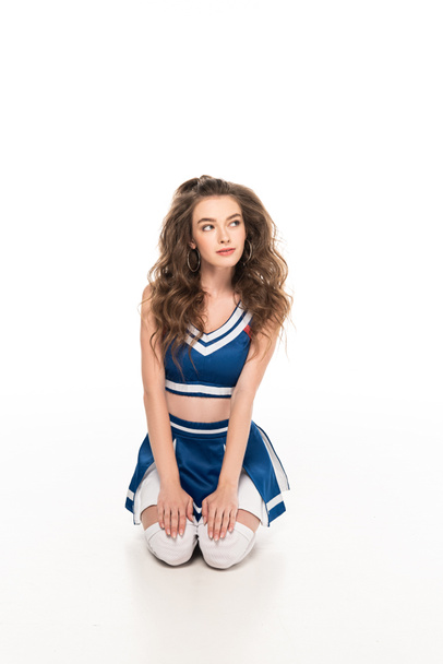 sexy dreamy cheerleader girl in blue uniform sitting on floor isolated on white - Photo, Image