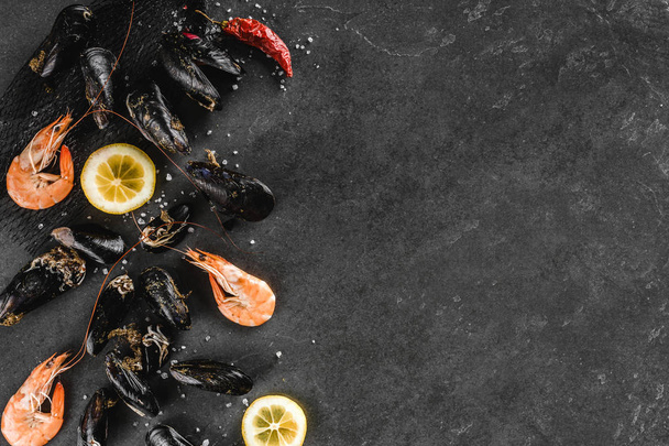 Fresh raw mussels and shrimp with spices and lemon on dark stone - Foto, Imagen