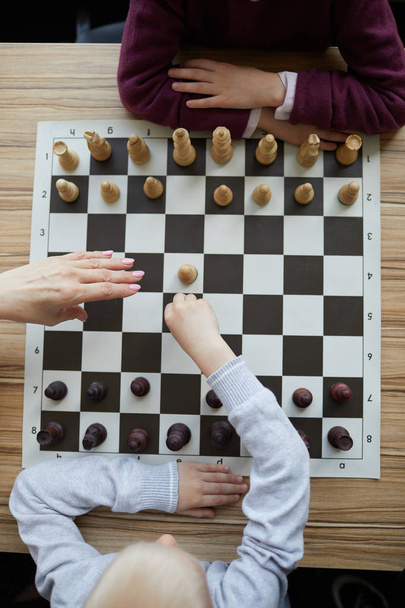 Die Hand des Lehrers über dem Schachbrett verhindert, dass der Junge einen falschen, gedankenlosen Schachzug macht - Foto, Bild