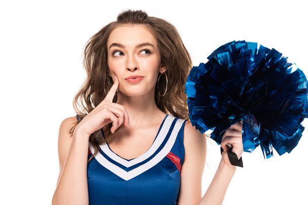 dromerige cheerleader meisje in blauw uniform vasthouden pompom en op zoek weg geïsoleerd op wit - Foto, afbeelding