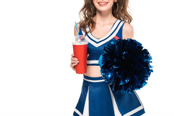 cropped view of happy cheerleader girl in blue uniform holding pompom and soda in paper cup isolated on white - Foto, Bild