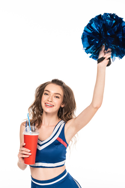 счастливая девушка чирлидер в синей форме держа помпон и газировку в бумажной чашке изолированы на белом
 - Фото, изображение