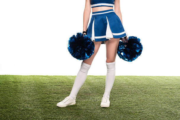 cropped view of sexy cheerleader girl in blue skirt and gaiters with pompoms on green field isolated on white - Photo, Image