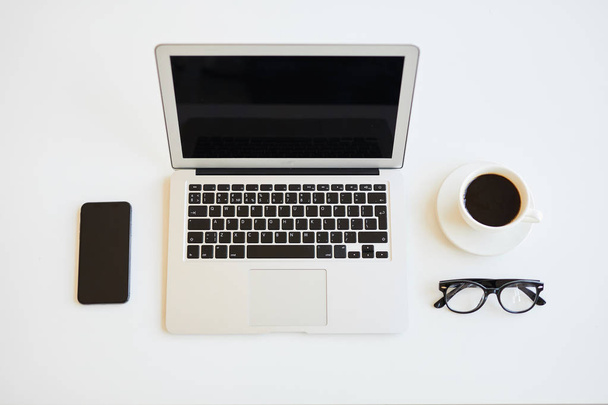 Direttamente sopra la vista della scrivania minimalista freelance con computer portatile aperto, tazza di caffè nero, occhiali e smartphone, colori in bianco e nero
 - Foto, immagini