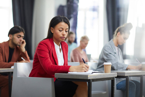 Portrait of contemporary mixed-race businesswoman taking notes in class during training course on business and management, copy space - Photo, Image