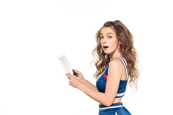 side view of shocked cheerleader girl in blue uniform holding digital tablet isolated on white - Foto, Bild