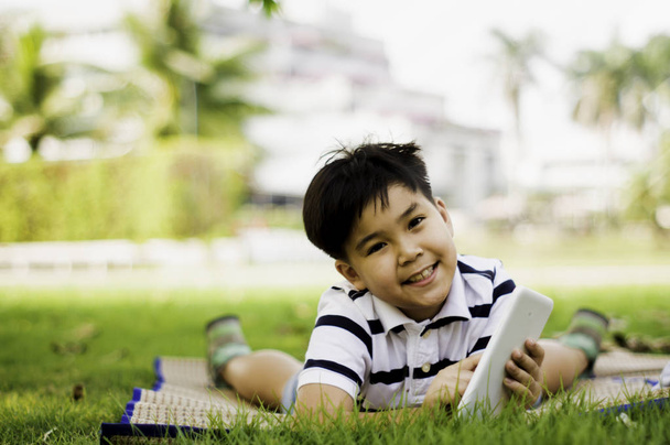 Азиатский мальчик с милой улыбкой, с табличкой в руке, стоя в саду
 - Фото, изображение