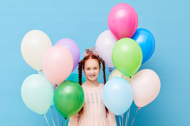 Taille up portret van schattige roodharige meisje houden ballonnen staande tegen pastel blauwe achtergrond, birthday party concept, ruimte kopiëren - Foto, afbeelding