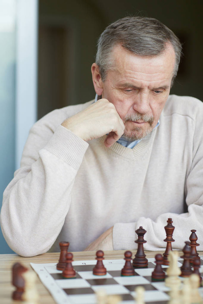 Velho mestre experiente perplexo com a testa enrugada e a barba cinzenta pensando cuidadosamente no próximo movimento de xadrez
 - Foto, Imagem