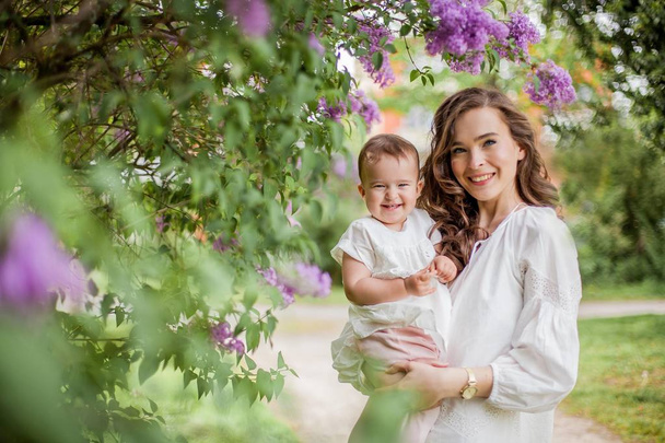 Hermosa joven madre e hija cerca de la floreciente lila. Primavera
. - Foto, Imagen