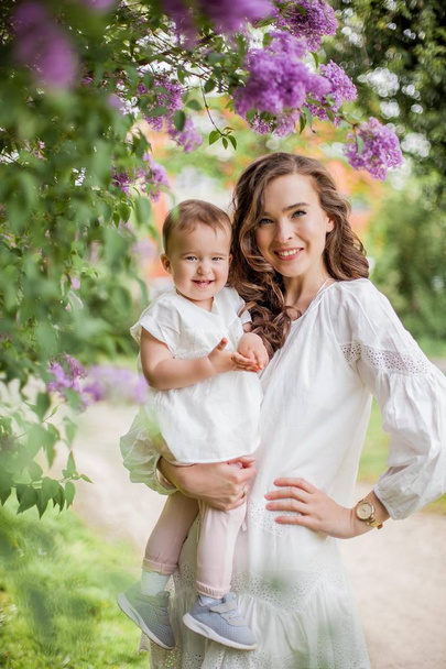 Beautiful young mother and daughter near the blossoming lilac. Spring. - Photo, Image
