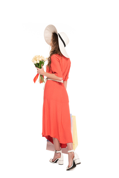 back view of elegant woman in hat and dress holding white tulips and shopping bags isolated on white - Foto, imagen