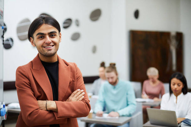 Waist up portrait of mixed-race young man smiling at camera confidently with group of students in background, copy space - Фото, изображение