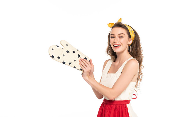 jonge gelukkige huisvrouw in jurk en schort houden oven Mitten geïsoleerd op wit - Foto, afbeelding