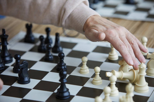Başarılı satranç hareketi yaptıktan sonra rakip satranç figürü almak eski satranç oyuncusunun kırışık eli - Fotoğraf, Görsel