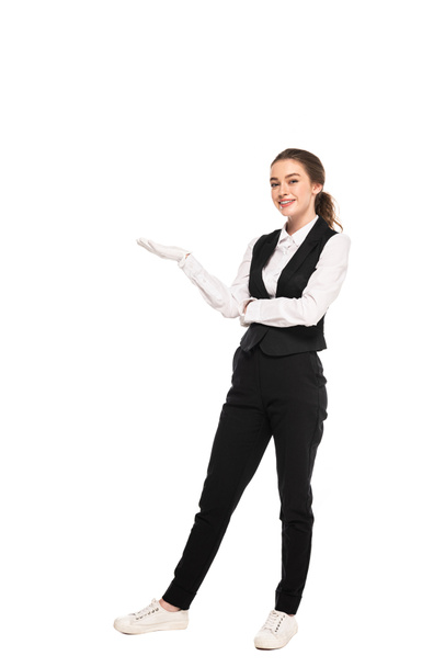 full length view of young waitress in formal wear and white gloves pointing with hand isolated on white - Foto, Imagen