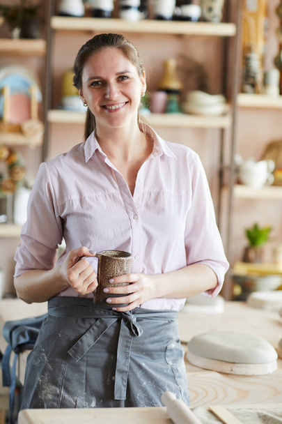Vita fino ritratto di allegra donna artigianale in posa in studio di ceramica tenendo tazza fatta a mano, spazio copia
 - Foto, immagini