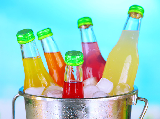 Bottles with tasty drinks in bucket with ice cubes, in bright background - Fotó, kép