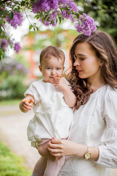 Bela jovem mãe e filha perto do lilás florescente. Primavera
. - Foto, Imagem