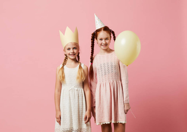 Portrait of two girls wearing party hats posing against pink background, copy space - Photo, Image