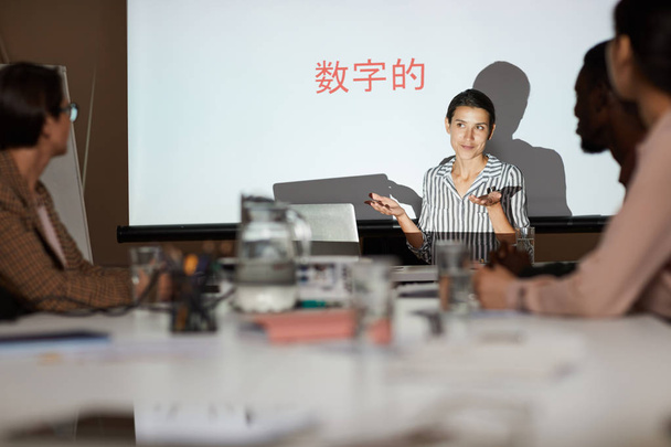 attraktive junge Frau gibt Schulungskurs über chinesische Kommunikation: Sie zuckt mit den Schultern, während sie bei einem Treffen Informationen erklärt - Foto, Bild