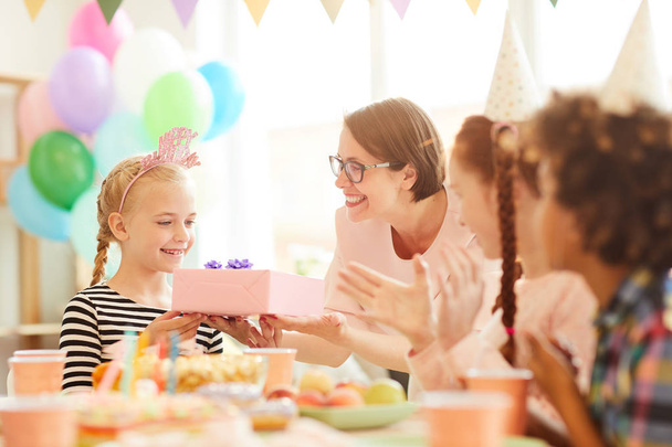 Portrait of cute little  girl  receiving gift from mom during Birthday party with friends, copy space - Photo, Image