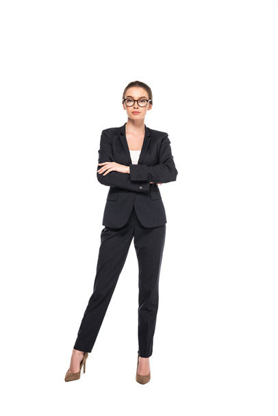 visão de comprimento total de jovem empresária bem sucedida em terno preto e óculos com braços cruzados isolados em branco
 - Foto, Imagem