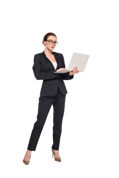 full length view of young successful businesswoman in black suit and glasses with laptop isolated on white - Zdjęcie, obraz