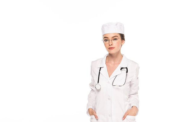 fiatal orvos fehér kabátot a sztetoszkóppal és a kezét a zsebek elszigetelt fehér - Fotó, kép
