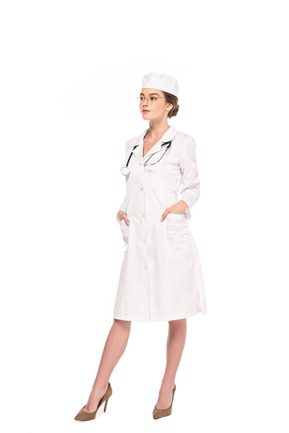full length view of young doctor in white coat with stethoscope posing with hands in pockets isolated on white - Fotoğraf, Görsel
