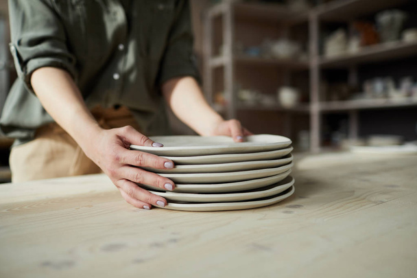 Крупный план неузнаваемой женщины-ремесленницы, держащей керамические плиты ручной работы в керамической мастерской, копировальное пространство
 - Фото, изображение