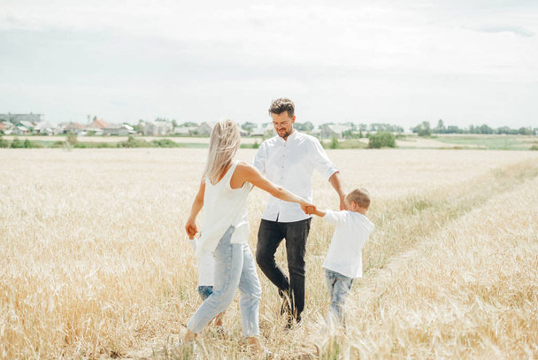 Щаслива сім'я з дітьми весело танцює, тримаючись за руки в пшеничному полі
. - Фото, зображення