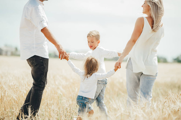Щаслива сім'я з чотирьох тримає руки танцює в колі на пшеничному полі
.  - Фото, зображення