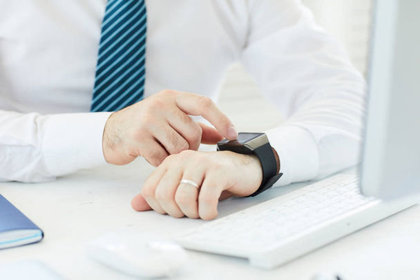 Close-up of unrecognizable businessman in white shirt sitting at desk with computer and reading message on smartwatch - Foto, afbeelding