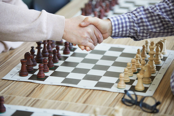 Twee man schudden handen boven tafel schaakbord en bril voorspel op schaaktoernooi - Foto, afbeelding
