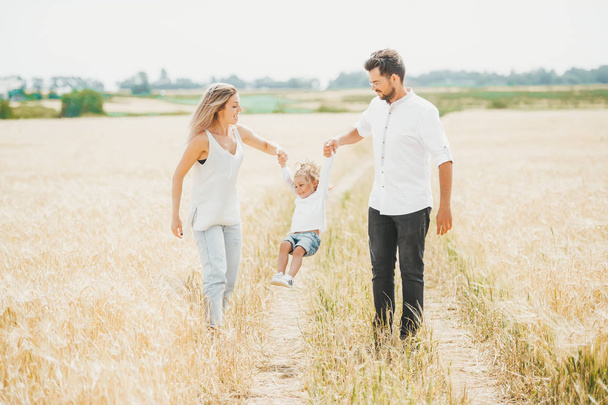 Cute little girl on walk with parent in wheat field on sunny day. Family vacation concept with copy space - Fotoğraf, Görsel