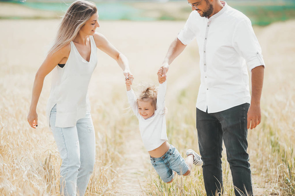 Mother, father and little girl having fun at the wheat field on a sunny day  - Foto, immagini